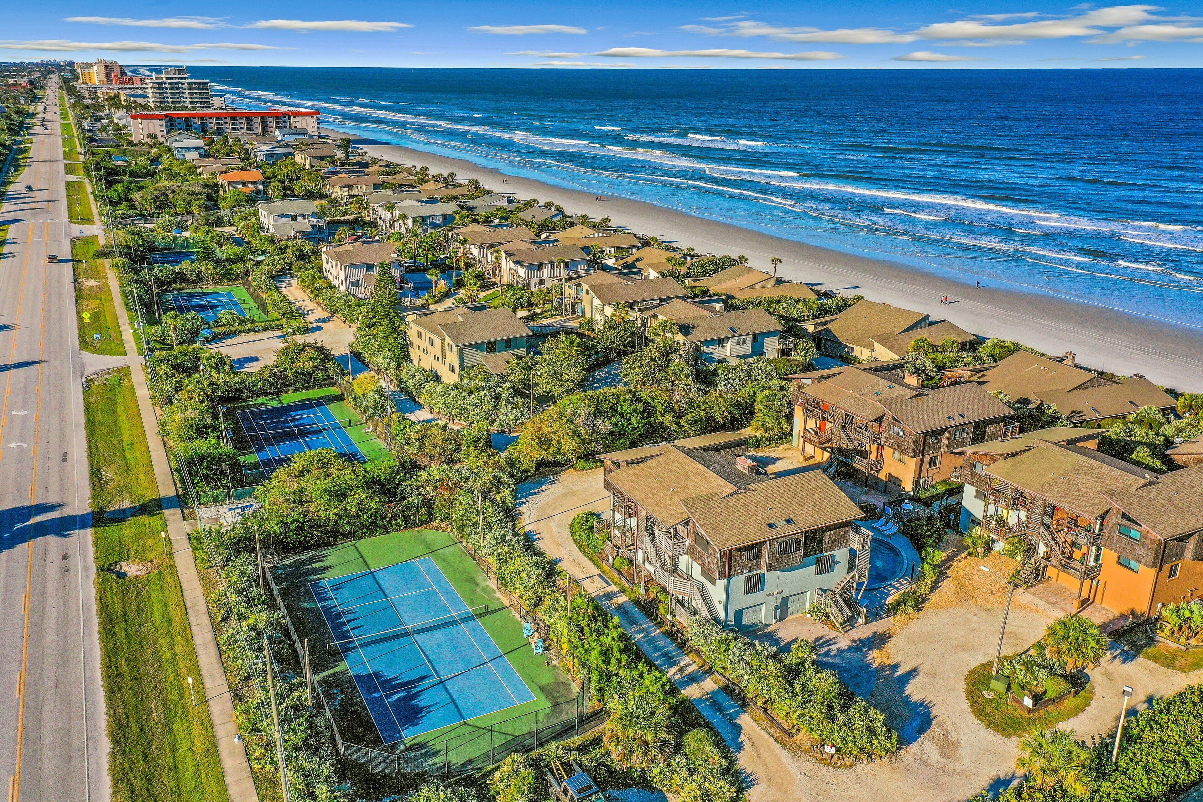 Un quartier résidentiel situé sur la côte, avec des propriétés donnant sur la plage, un court de tennis et une route parallèle à la plage.