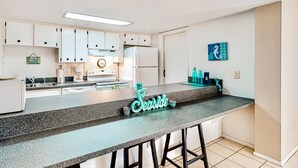 A modern kitchen with white cabinets, a granite countertop, and a 'Seaside' sign. - Oceanfront Condo with Pool & Patio – Peaceful Beachside Vibes (New Smyrna Beach)