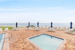 A rooftop pool area with lounge chairs and umbrellas, overlooking a beach. - Oceanfront Condo with Pool & Patio – Peaceful Beachside Vibes (New Smyrna Beach)