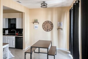 A kitchen with white cabinets, a black countertop, and a red pot. There is a dining area with a wooden table and benches. - Oceanfront Condo w/ Balcony, Pool & Serene Beach Access (New Smyrna Beach)