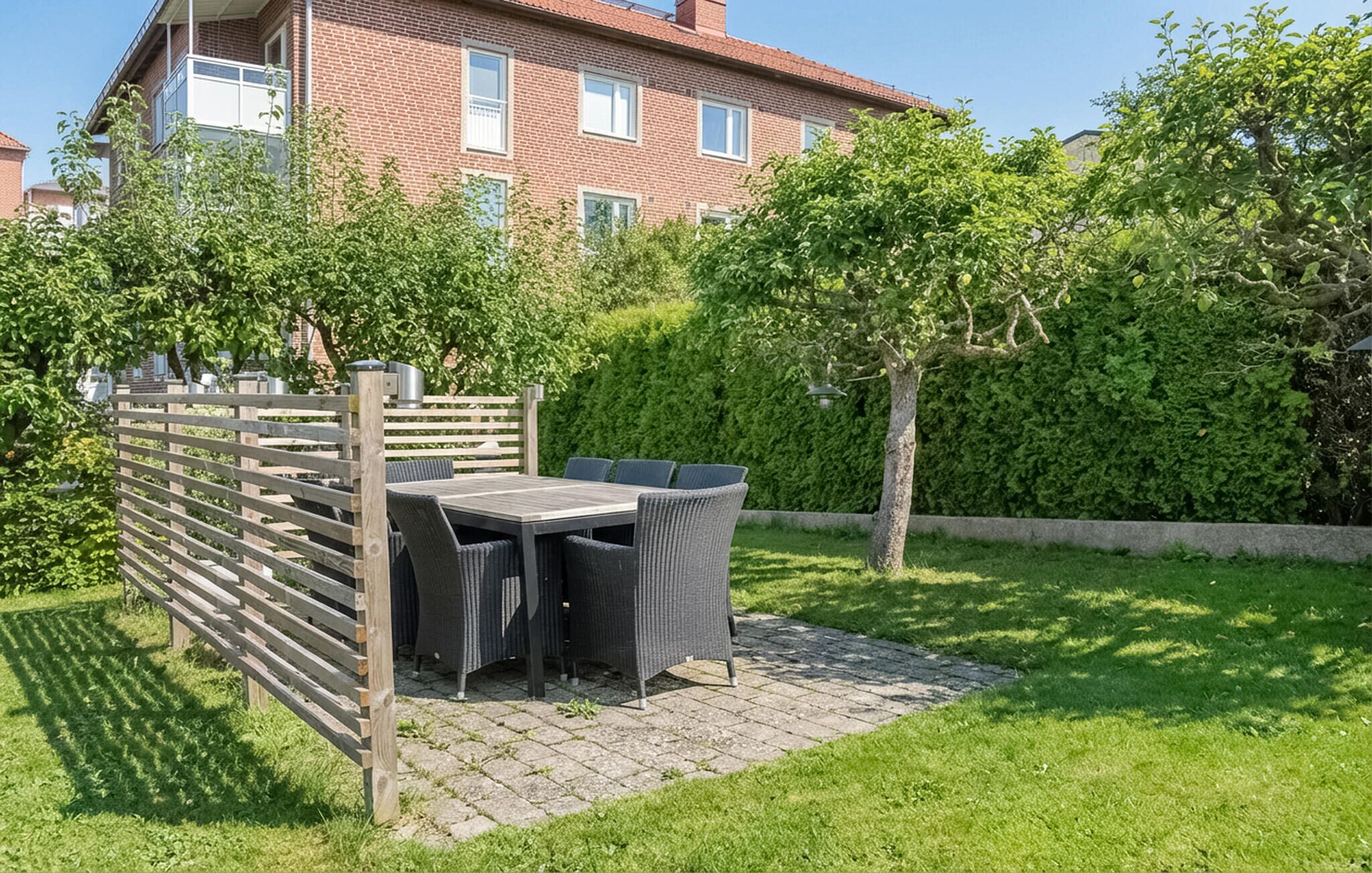A patio with a table and chairs, surrounded by a wooden fence and lush greenery.