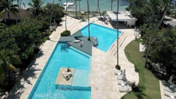 A resort with a large pool, palm trees, and a view of the ocean. - A paradise in the Caribbean (Playa Juan Dolio)