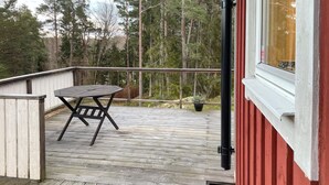 Eine Holzterrasse mit Tisch und Stühlen, umgeben von einem Geländer und einem roten Gebäude.