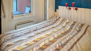 Ein Schlafzimmer mit einer gesteppten Bettdecke, einem Fenster mit Blick und einer wandmontierten Lampe.
