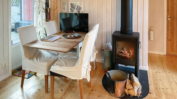 Ein gemütliches Zimmer mit einem Holztisch, weißen Stühlen, einem schwarzen Fernseher und einem Kaminofen.