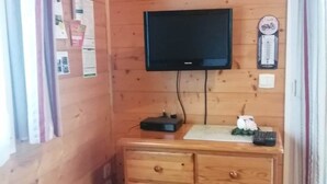 A wooden cabin room with a television mounted on the wall, a small wooden table, and a cabinet with drawers. - Lilie's Chalet, a farm stay (BASSIGNAC)
