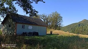 A small house with a sloped roof, a window, and a door, surrounded by greenery and hills. - Lilie's Chalet, a farm stay (BASSIGNAC)