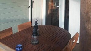 A wooden table with chairs, a bottle, and a lantern in a covered outdoor area with a sliding glass door. - Lilie's Chalet, a farm stay (BASSIGNAC)