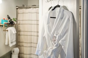 A white bathrobe hanging on a hook in a bathroom with a shower curtain, a towel rack, and toiletries.