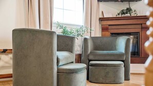 Een kamer met een houten vloer, een open haard en twee grijze fauteuils.