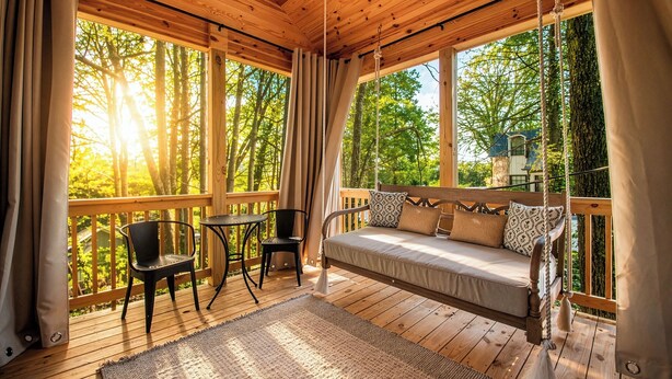 Een houten terras met een bank, stoelen en een tafel, met uitzicht op een bebost gebied.