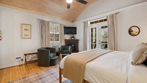 Een slaapkamer met een bed, een plafondventilator, een open haard en een raam met gordijnen.