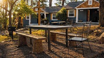 A rustic outdoor seating area with a table and benches, surrounded by trees and a building with a sign reading 'CINNAMON LAND'.