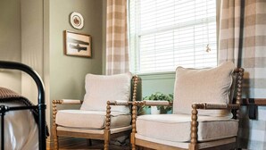 A room with two wooden armchairs, a framed picture on the wall, and a window with blinds.