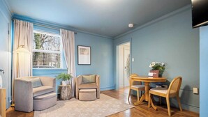 A room with a blue wall, a round wooden table with chairs, a sofa, a small side table with a plant, and a window with curtains. - Etowah Suite w Hot Tub, Family Stay Near Rock City (Lookout Mountain)