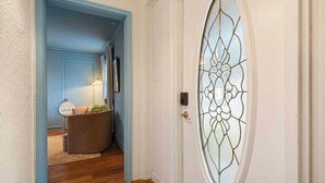 A hallway with a blue door, a round glass door with a geometric pattern, a brown ottoman, and a 'Welcome' sign. - Etowah Suite w Hot Tub, Family Stay Near Rock City (Lookout Mountain)