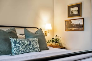 Una cama con almohadas, una lámpara de pared y dos cuadros enmarcados.
