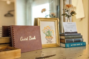 Un libro de visitas marrón, una obra de arte floral enmarco y una pila de libros sobre una superficie de madera.