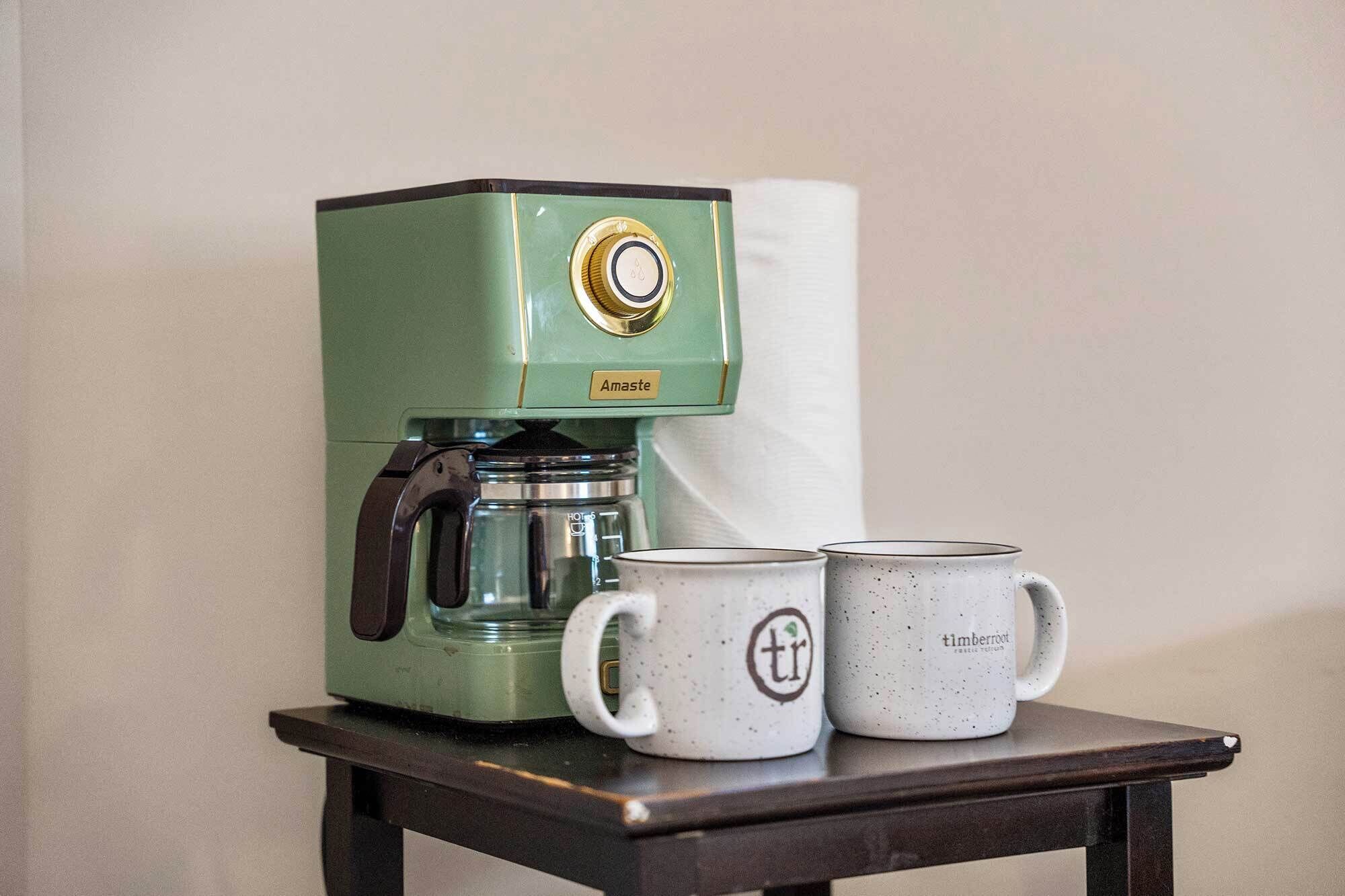 Una máquina de café verde con dos tazas blancas sobre una mesa pequeña.