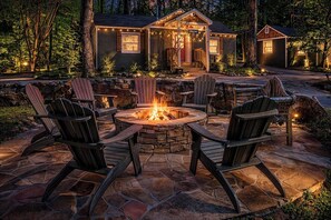 A stone fire pit with chairs, a wooden deck, and a house with string lights. - Laurel Falls Suite on Lookout Mountain (Lookout Mountain)