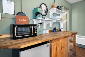 Een keuken met een magnetron, koffiezetapparaat en een kleine koelkast. Op het aanrecht ligt een gastenboek, en daarboven staan planken met verschillende spullen.