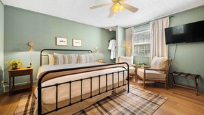 Un dormitorio con cama, ventilador de techo, ventana con persianas, una silla y televisor.