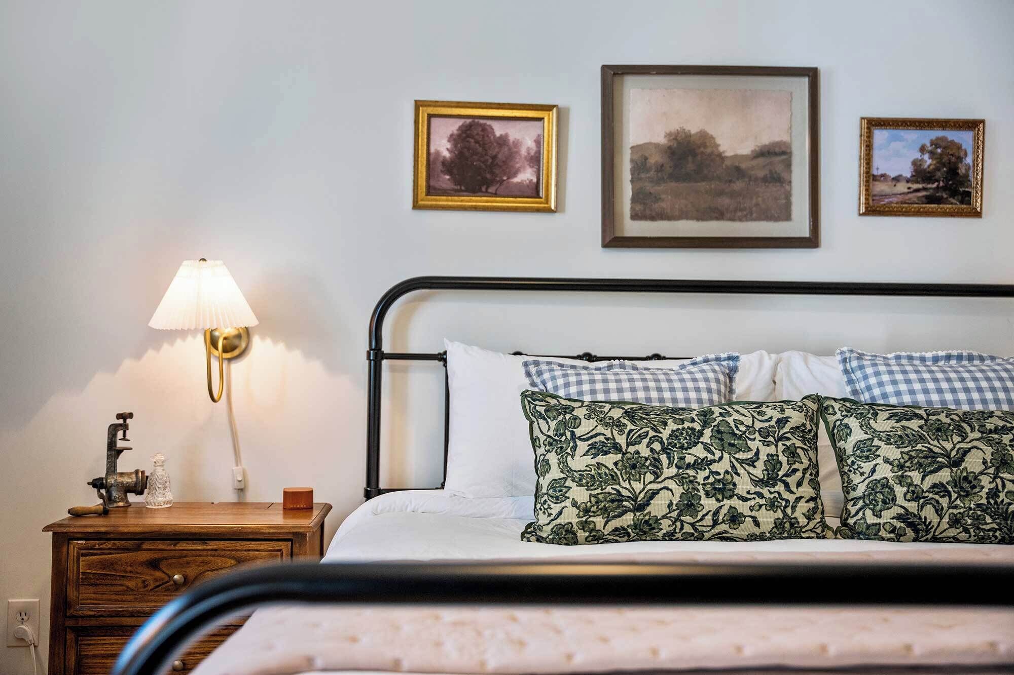 Een slaapkamer met een bed, een nachtkastje met een lamp en drie ingelijste foto’s aan de muur.