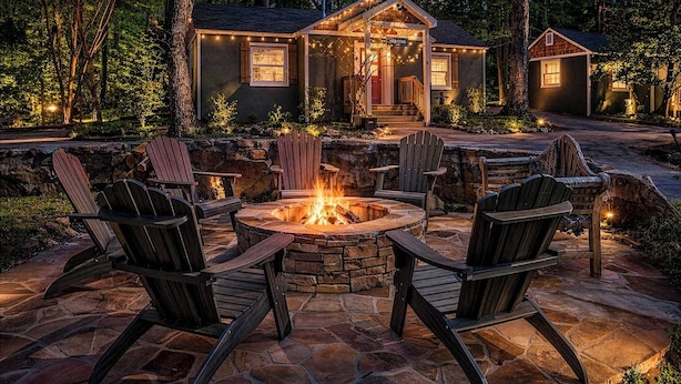 Un foyer en pierre entouré de chaises, une terrasse en bois et une maison décorée de guirlandes lumineuses.