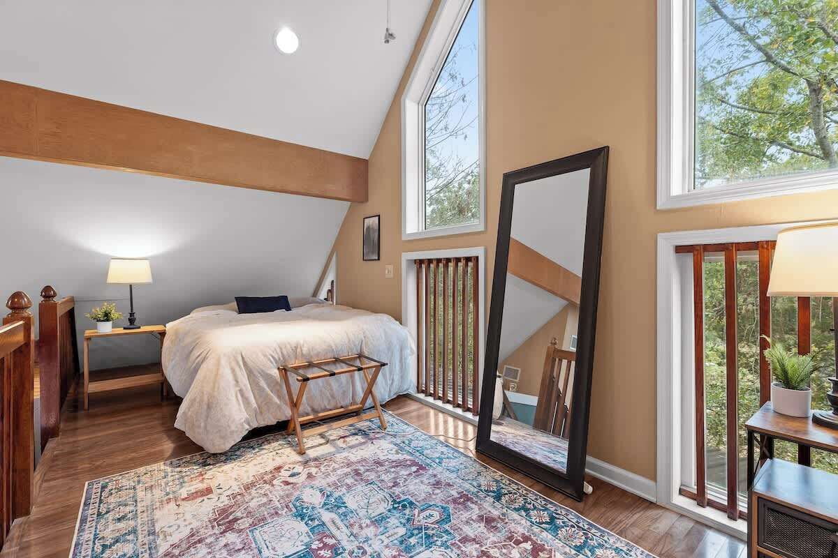 Une chambre avec un grand lit, un banc en bois, un miroir et une vue sur l’extérieur.