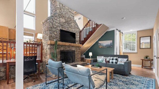 Una sala de estar con chimenea de piedra, un sofá, una mesa de centro y una escalera.