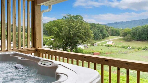 Un bain à remous sur une terrasse en bois, avec vue sur un paysage verdoyant et des collines.