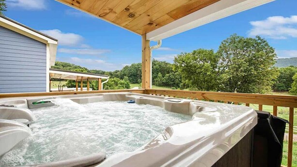 A hot tub with a wooden deck and a view of a house and trees. - The Honeycomb Cabin (Chattanooga)