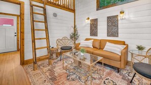 A cozy room with a wooden ladder, a sofa, a glass coffee table, and a patterned rug. - The Honeycomb Cabin (Chattanooga)