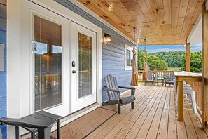 Eine überdachte Veranda mit Holzterrasse, einer Schiebetür und Blick auf einen bewaldeten Bereich.
