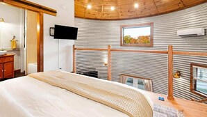 A bedroom with a bed, wooden ceiling, a mounted TV, and a window with a view. - Lookout Silo with Mountain Views & Hot Tub (Chattanooga)