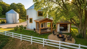 Eine rustikale Holzhütte mit einem großen Metallsilobunker, einer Holzterrasse und einem Feuerstellenbereich.