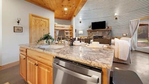 A modern kitchen with granite countertops, wooden cabinetry, a built-in dishwasher, and a stone fireplace. - Cozy Ridge Silo - Sleeps 6 with Private Hot Tub (Chattanooga)