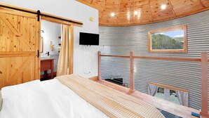 A bedroom with a wooden ceiling, a bed, a TV, a window, and a view of the outdoors. - Cozy Ridge Silo - Sleeps 6 with Private Hot Tub (Chattanooga)