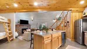 A spacious kitchen with wooden cabinets, a central island, a stone fireplace, and a modern refrigerator. - Cozy Ridge Silo - Sleeps 6 with Private Hot Tub (Chattanooga)