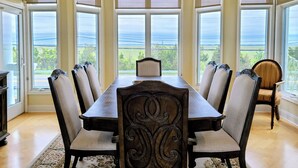 Ein Esszimmer mit langem Tisch und sechs Stühlen, großen Fenstern mit Aussicht und einem Deckenventilator.