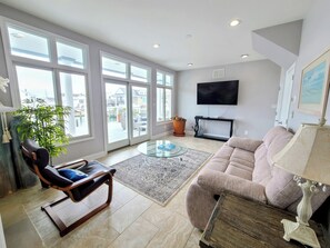 Ein Wohnzimmer mit einer Couch, einem Glastisch, einem Fernseher und einem großen Fenster.
