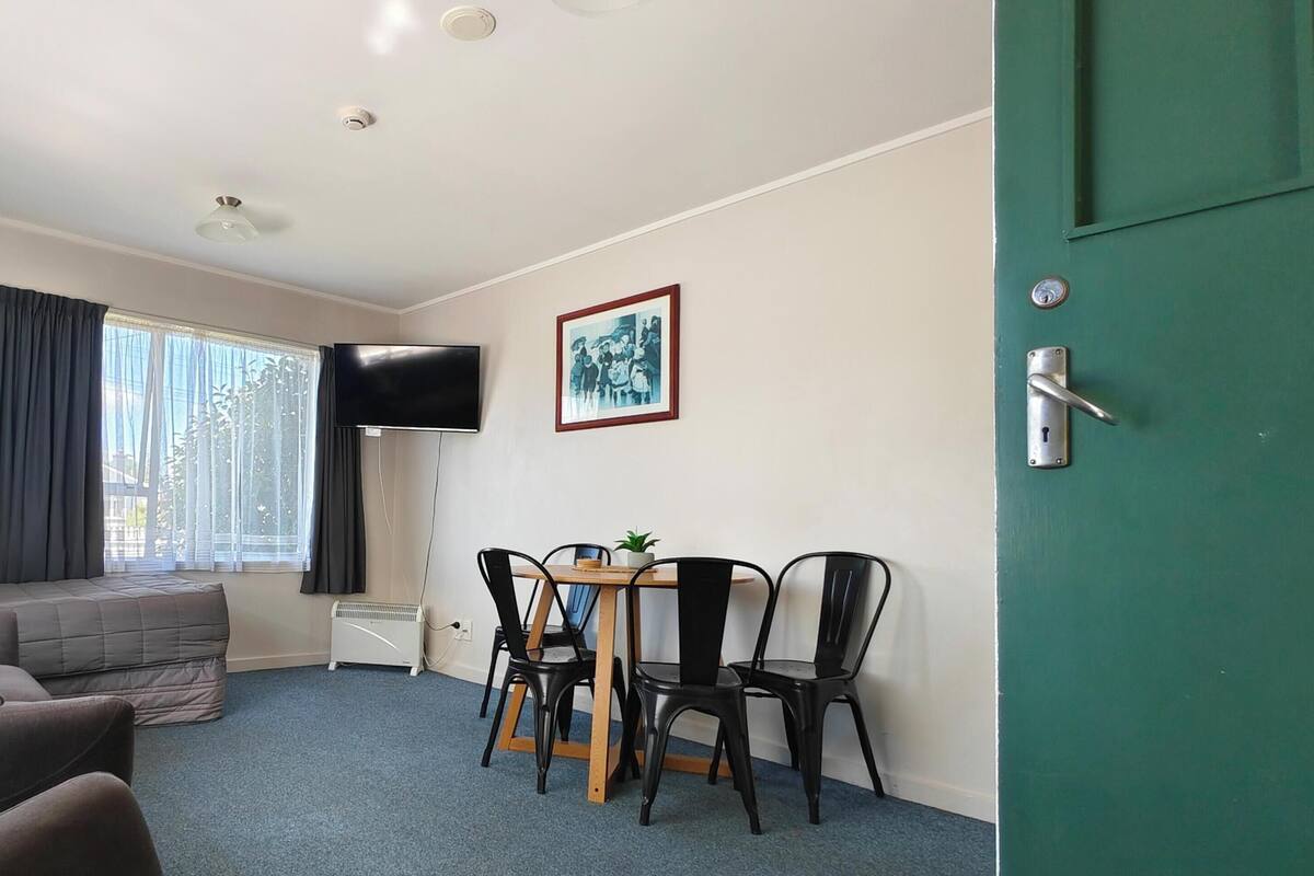Una habitación con sofá, una mesa con sillas, televisión y un cuadro en la pared.