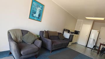 A living room with two sofas, a framed picture on the wall, a kitchenette, and a door leading to another room.