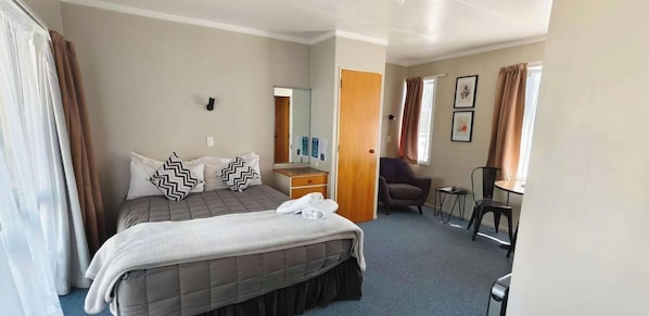 A hotel room with a bed, a desk, a chair, and a small table.