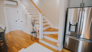 A modern kitchen with a stainless steel refrigerator, wooden staircase, and a white door. - The Creek House on Kaaterskill (Palenville)