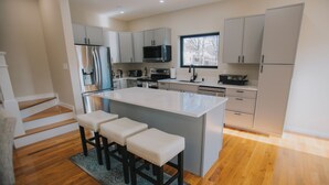 A modern kitchen with a central island, bar stools, stainless steel appliances, and light-colored cabinetry. - The Creek House on Kaaterskill (Palenville)