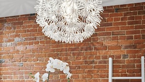 A modern room with a glass table, a cushioned chair, a white chandelier, and a brick wall. - Modern Heritage Apartment in the Heart of Halifax (Halifax)