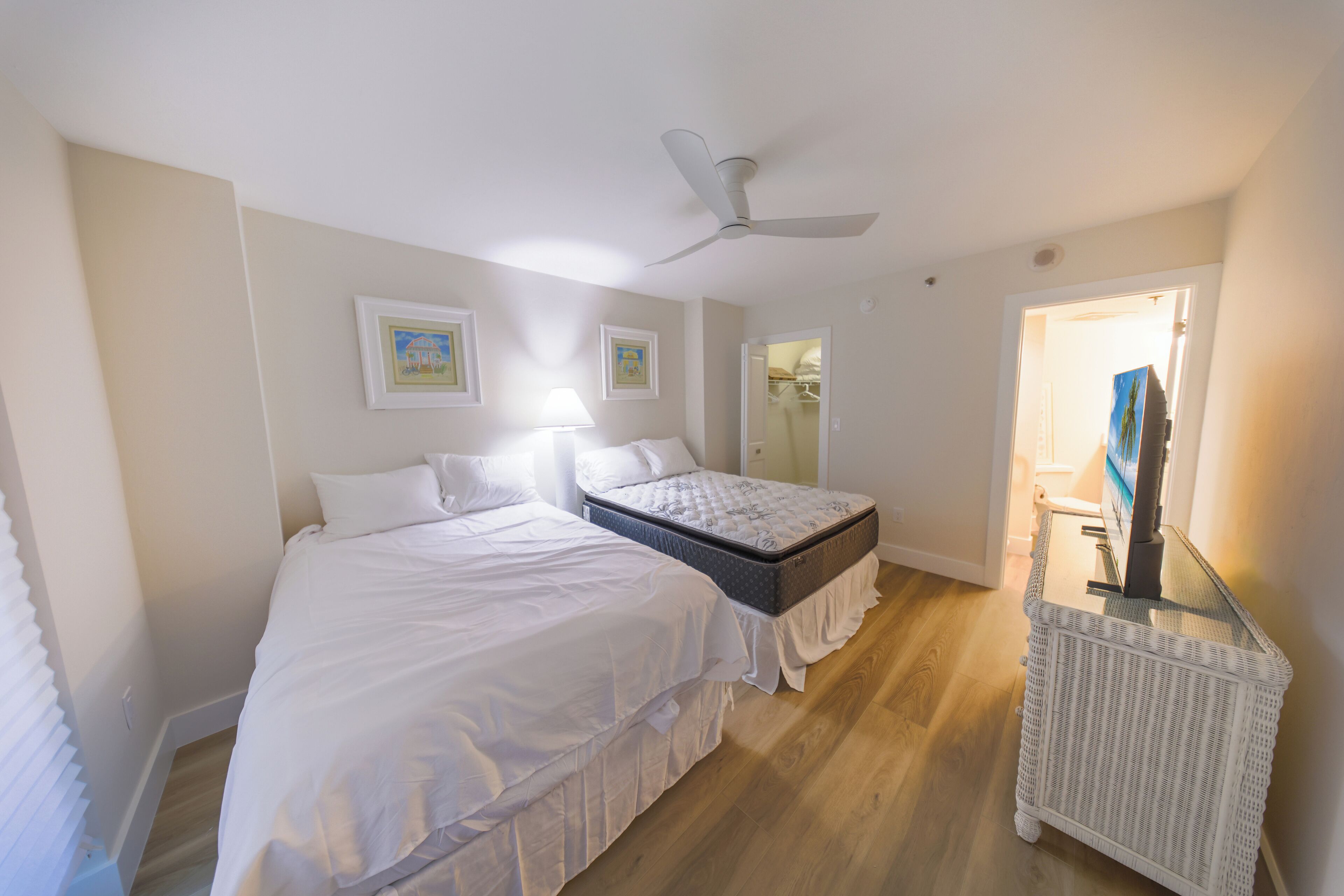A bedroom with two beds, a ceiling fan, a bedside table, and a walk-in closet.