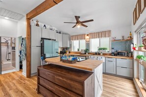 A modern kitchen with a wooden island, white cabinets, and a ceiling fan. - Hale Kekio (Kaaawa)