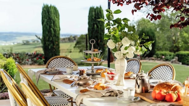 An outdoor dining area with a table set for breakfast, surrounded by chairs, and a view of the countryside. - One-of-a-Kind French Farm Stay in Kiama Hinterland (Jerrara)